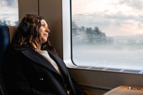 Kvinna med hörlurar som tittar ut genom tågfönstret.